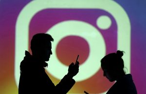 Silhouettes of mobile users are seen next to a screen projection of Instagram logo in this picture illustration