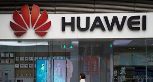 A woman walks by a Huawei logo at a shopping mall in Shanghai