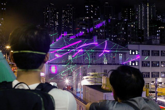 Anti-extradition bill protesters watch as demonstrators point laser pens at the police station in Sham Shui Po in Hong Kong