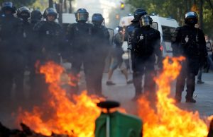 Riot police officers stand next to a burning barricade during a protest urging authorities to take emergency measures against climate change, in Paris