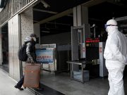 A worker in protective suit looks at a man while he enters the Xizhimen subway station, as the country is hit by an outbreak of the new coronavirus, in Beijing