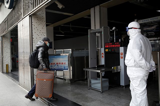 A worker in protective suit looks at a man while he enters the Xizhimen subway station, as the country is hit by an outbreak of the new coronavirus, in Beijing