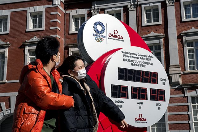 A couple wearing protective face masks, following an outbreak of the coronavirus, walk past the big Omega One-Year Countdown clock for the opening ceremony of the Tokyo 2020 Olympic outside of Tokyo Station in Tokyo